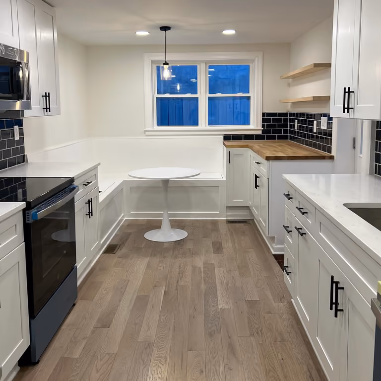 White kitchen with island, white cabinets, wood floor and blue dusk at the rear window.