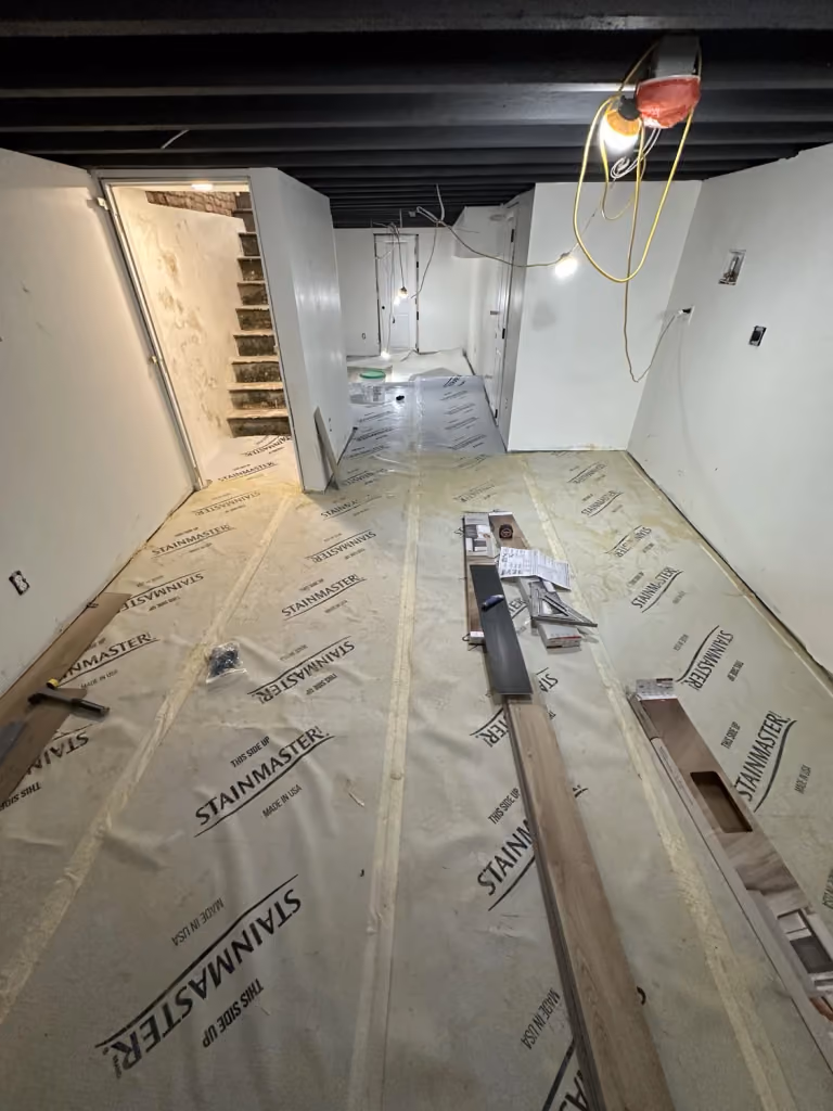 Installing basement flooring beneath the exposed dark ceiling.