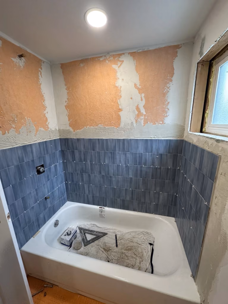Blue wall tile being installed around the tub.