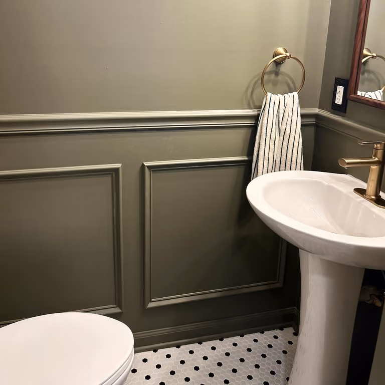 Olive powder room with white basin, painted wainscoting and a towel on warm metallic hardware.